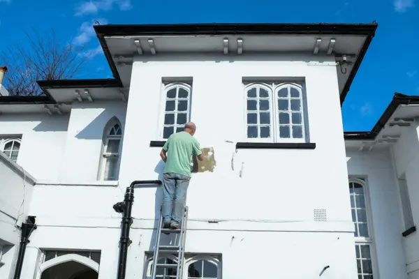 Pintor sobre una escalera pintando el frente blanco de una casa